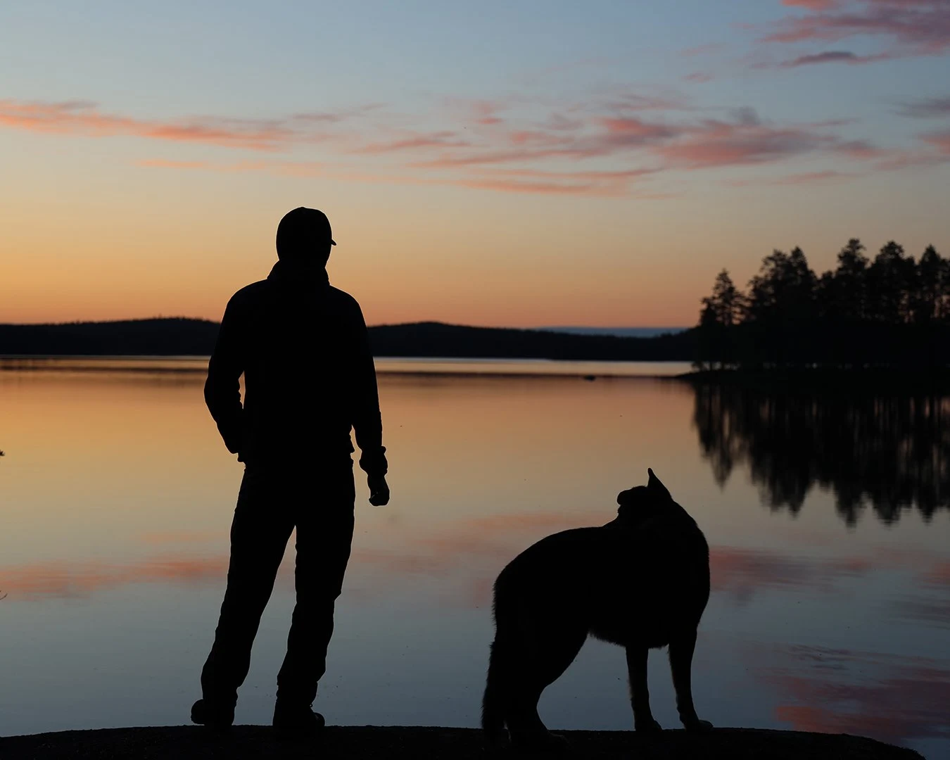 Ihmisen ja koiran siluetit järven rannalla auringonlaskussa